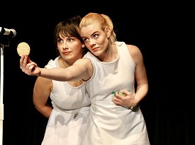 A dancer in white holding out a round cookie in front of another dancer