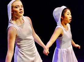 Two dancers in white hoods holding hands