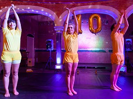 Three performers in yellow with arms above their heads