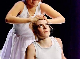 A dancer in white pressing another dancer towards the ground